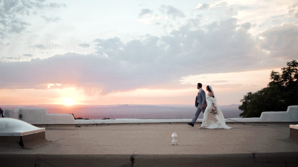 man and woman walking across a roof with sunset background