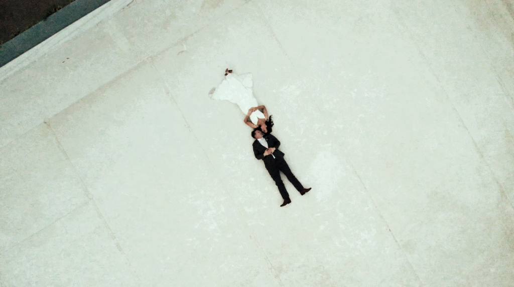 overhead drone shot of a bride and groom laying down on a rooftop