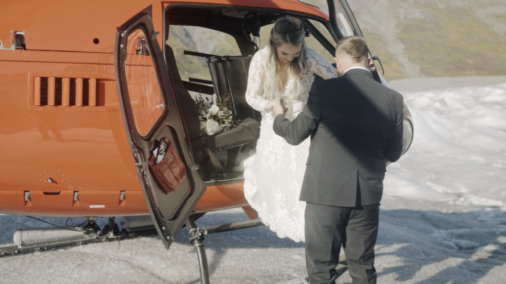 groom helping his bride out of a red helicopter